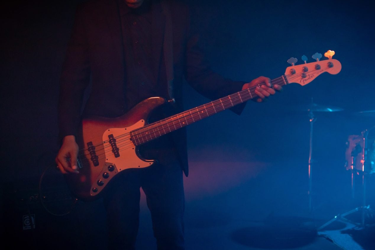 Photo of a sunburst Jazz Bass being played on a dark stage.