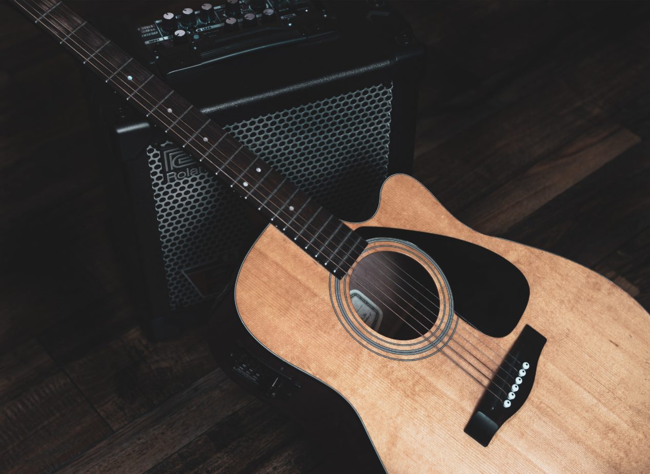 Photo from above of an acoustic guitar resting against an amp.