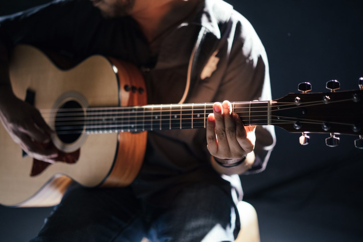 Photo of a man playing an acoustic guitar against a dark background.