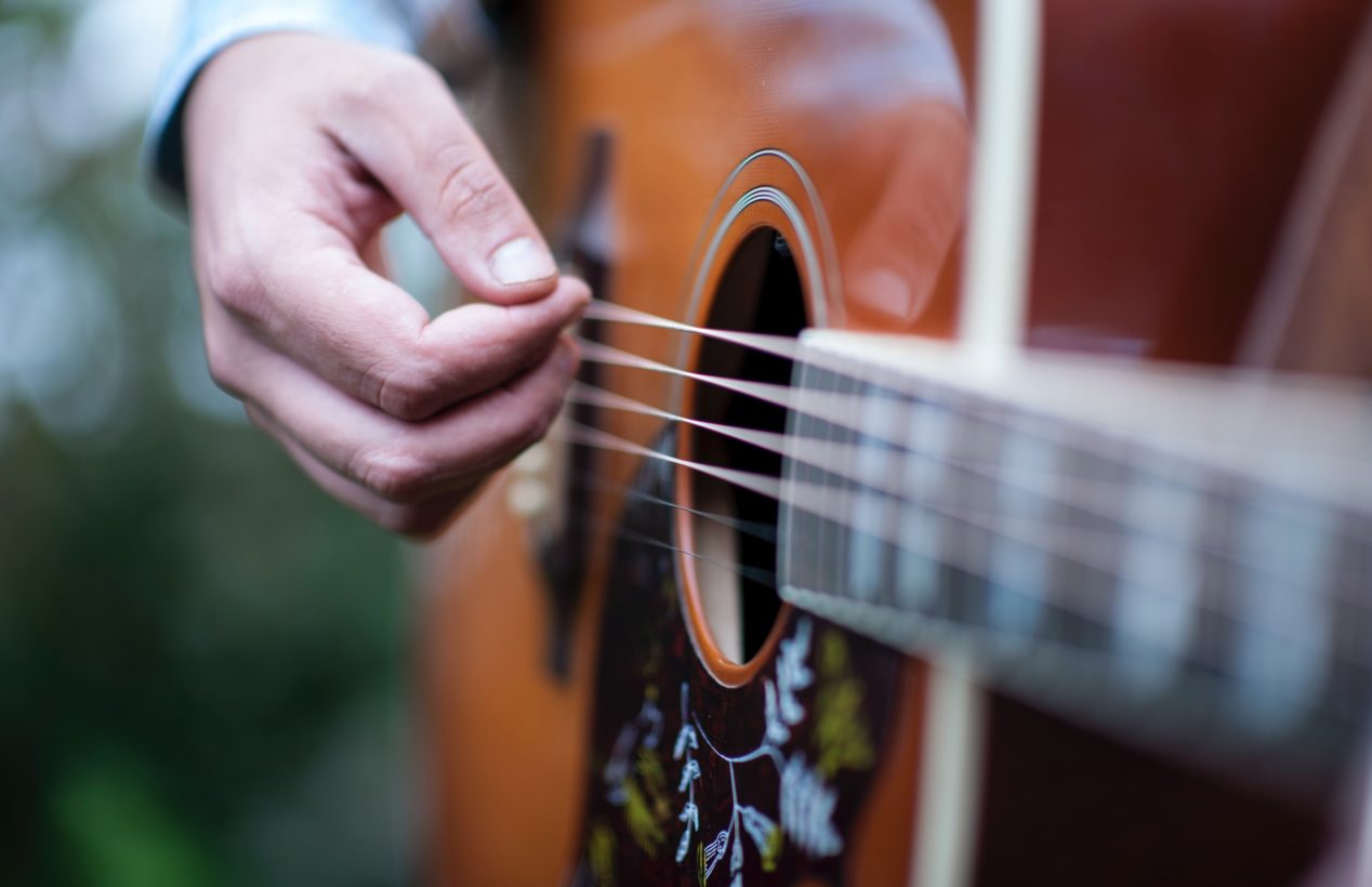 Photo of a man playing an acoustic guitar outside.