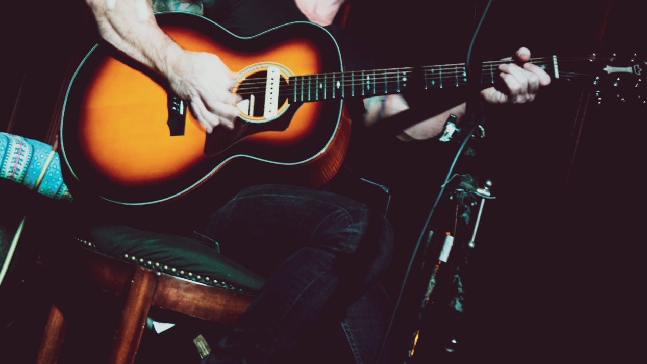 Photo of a man playing a parlor sized acoustic guitar on stage.