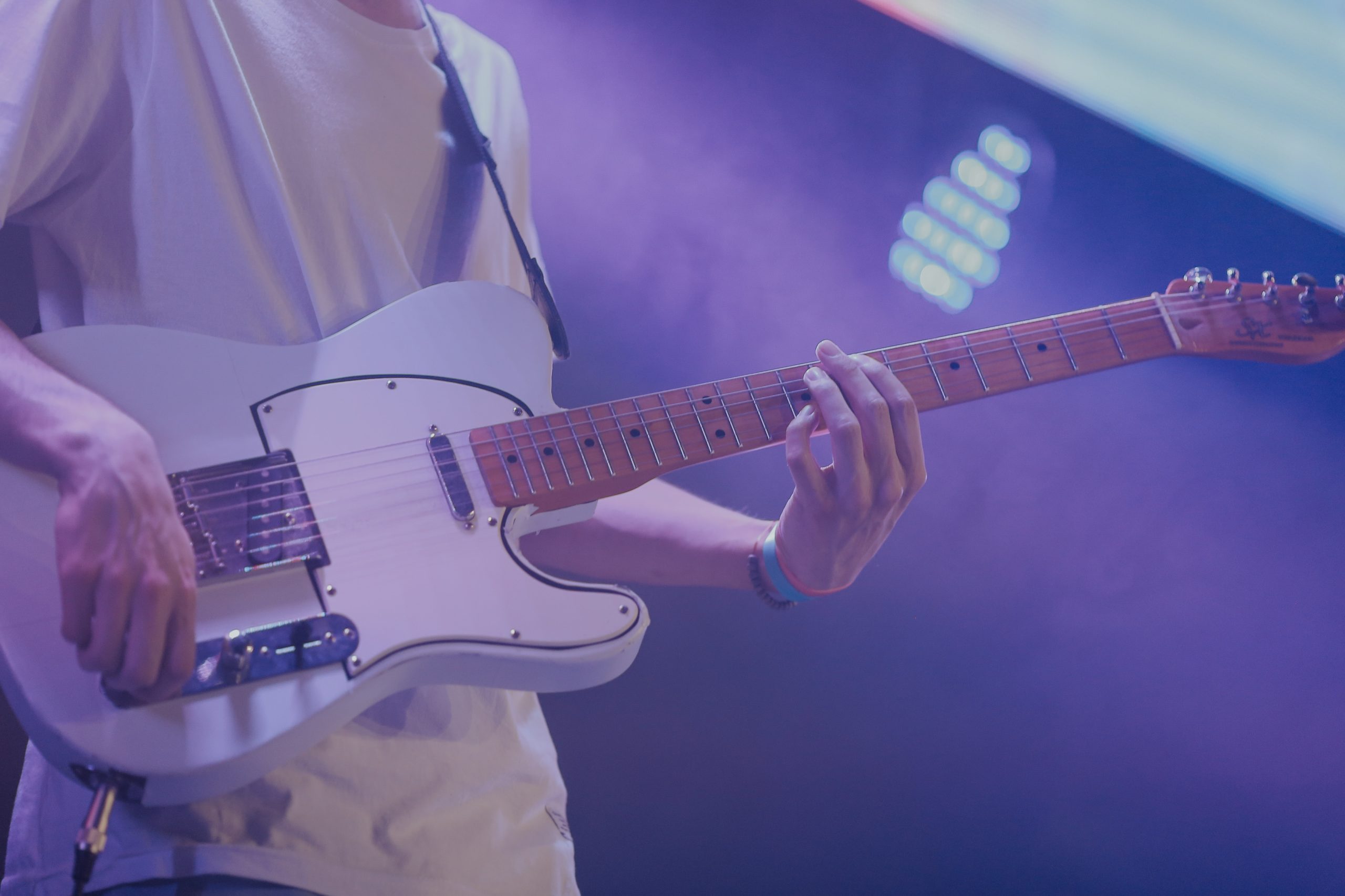 Photo of a man playing a white telecaster on stage.