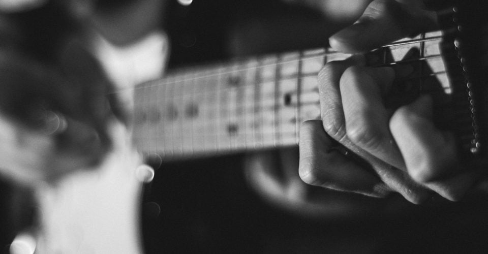A black and white close up photo of someone playing a Stratocaster.